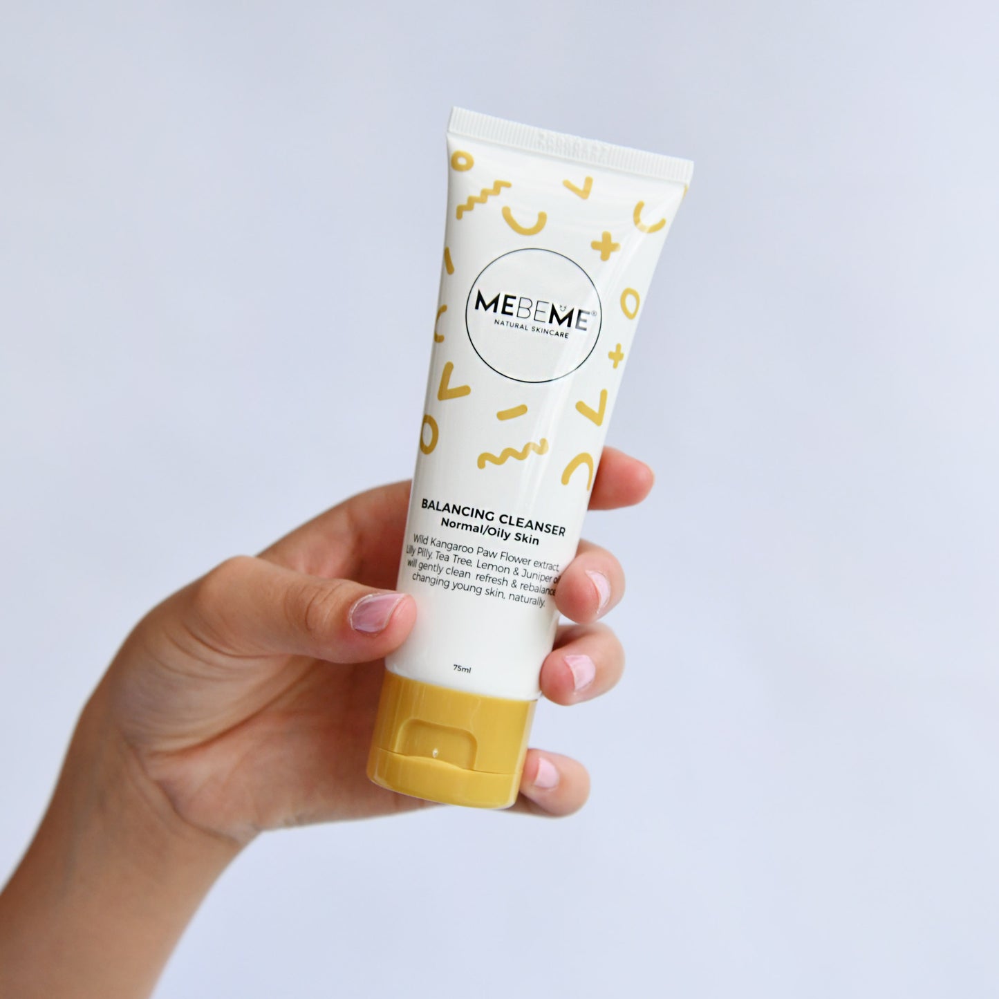 Hand holding a tube of MEBEME skincare product against a light gray background
