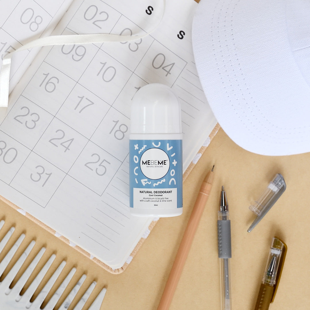 A bottle of natural deodorant Cool Coconut by MEBEME placed on a desk with stationery items, a calendar, and an notepad.