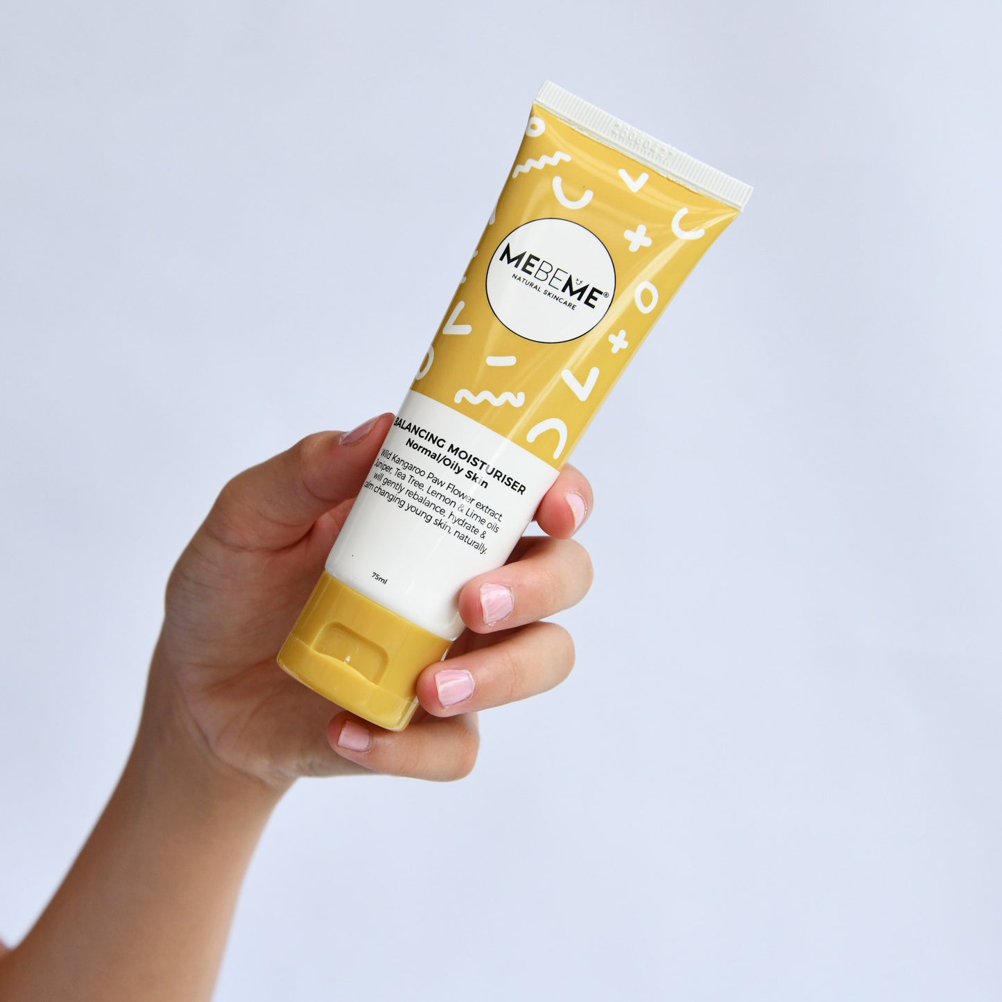 Hand holding a yellow and white tube of MEBEME product against a light gray background
