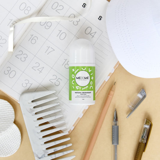 A bottle of natural deodorant with a green label, positioned on a desk surrounded by office supplies and a skincare routine schedule.
