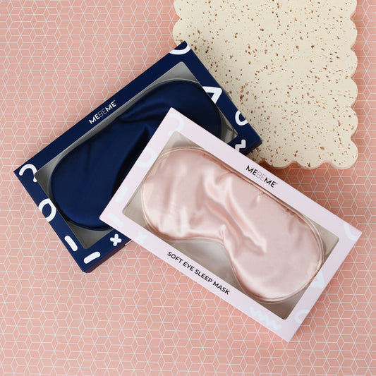 Pink eye sleep mask in packaging and navy eye sleep mask on a pink geometric patterned background