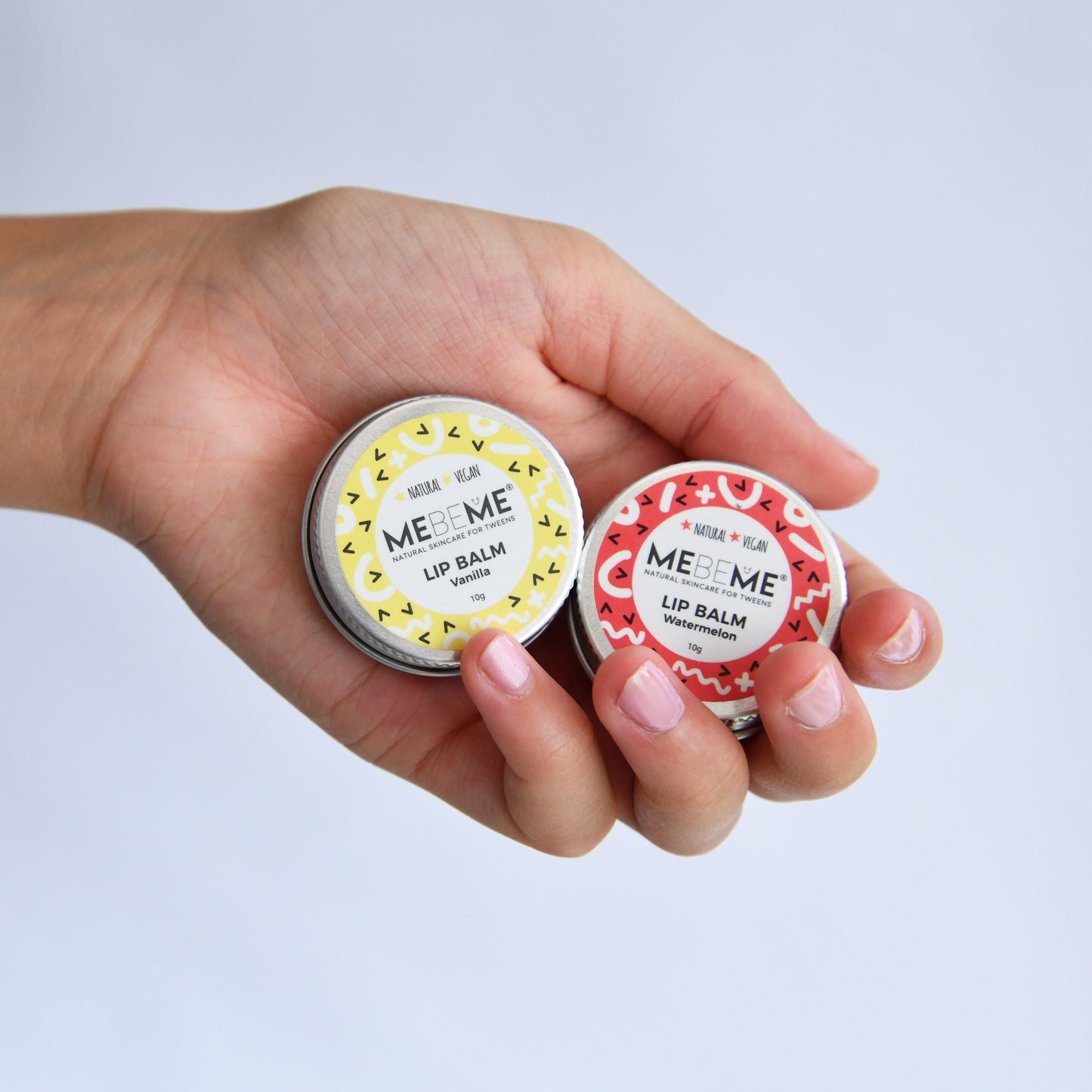 Hand holding two MEBEME lip balm containers against a light gray background