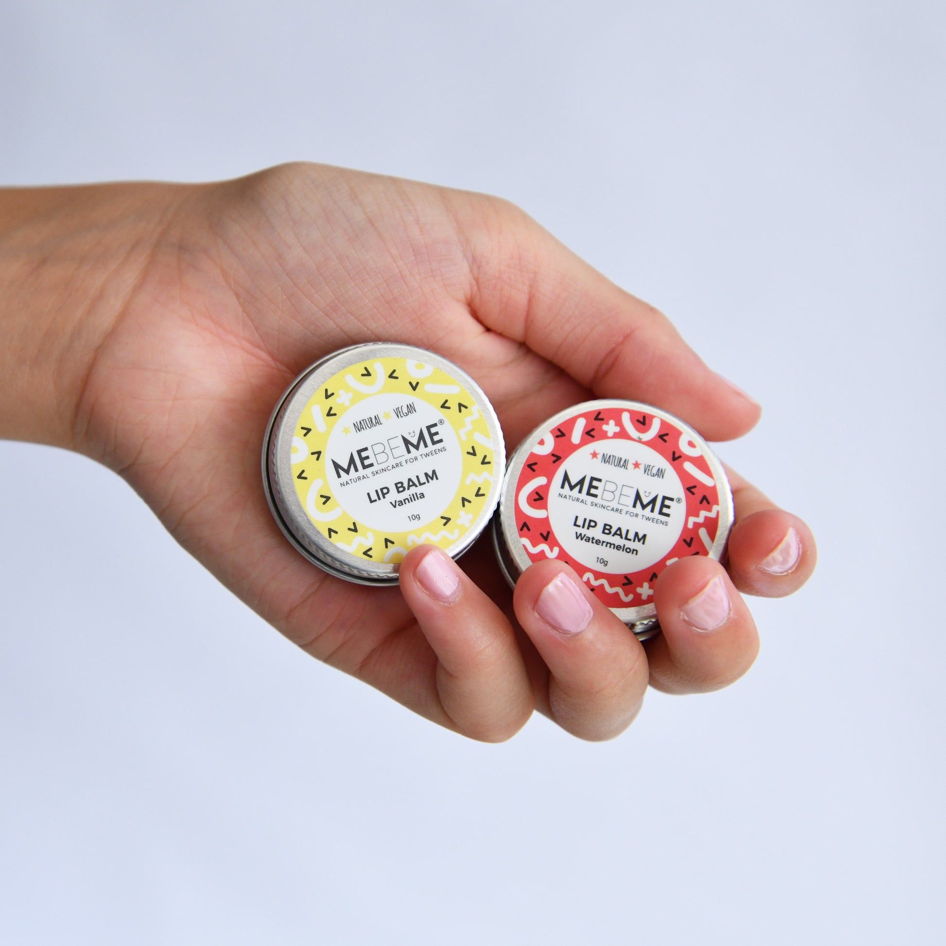 Hand holding two MEBEME lip balm containers against a light gray background