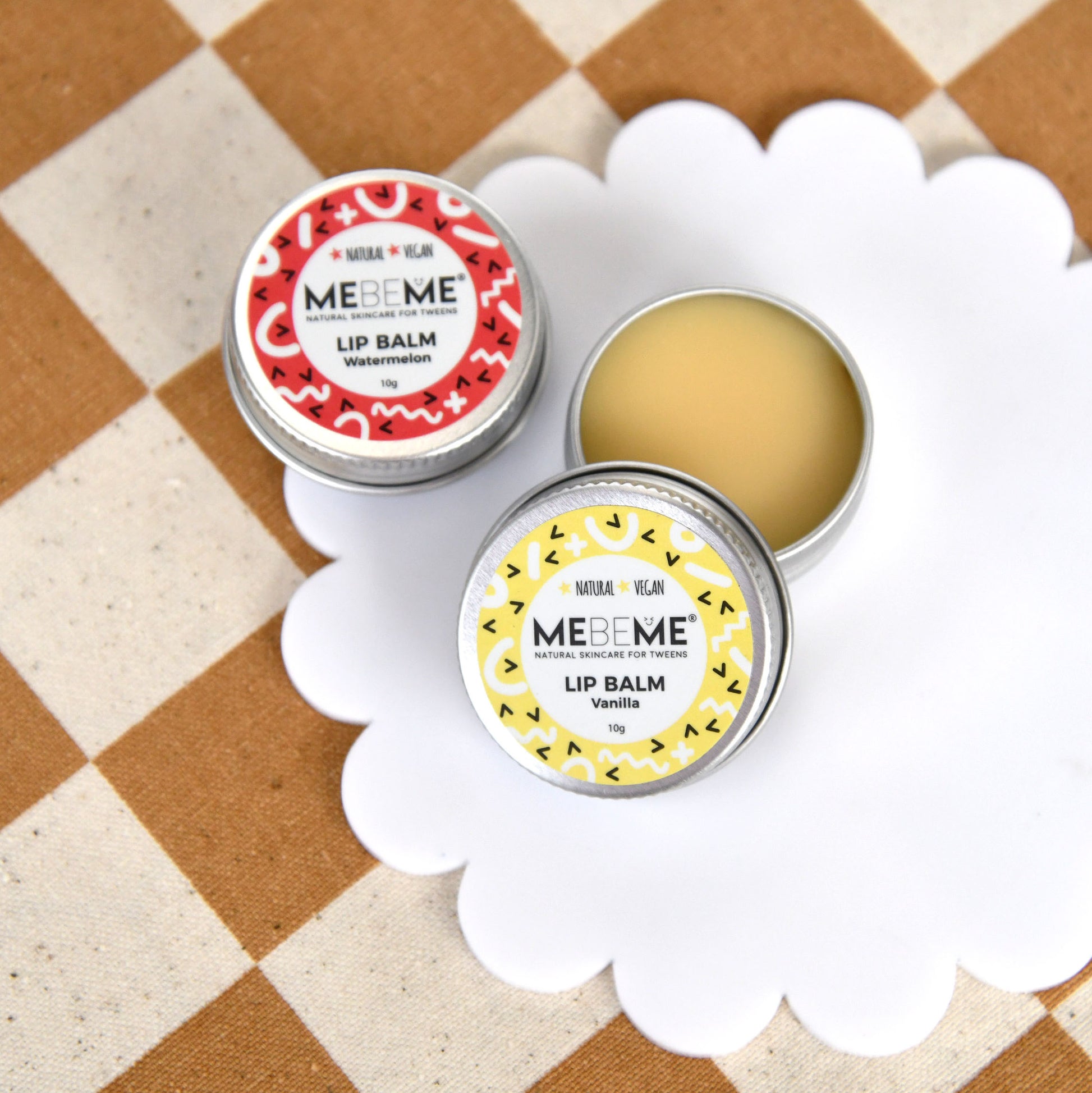 Two ME BE ME lip balm tins on a checkered fabric background