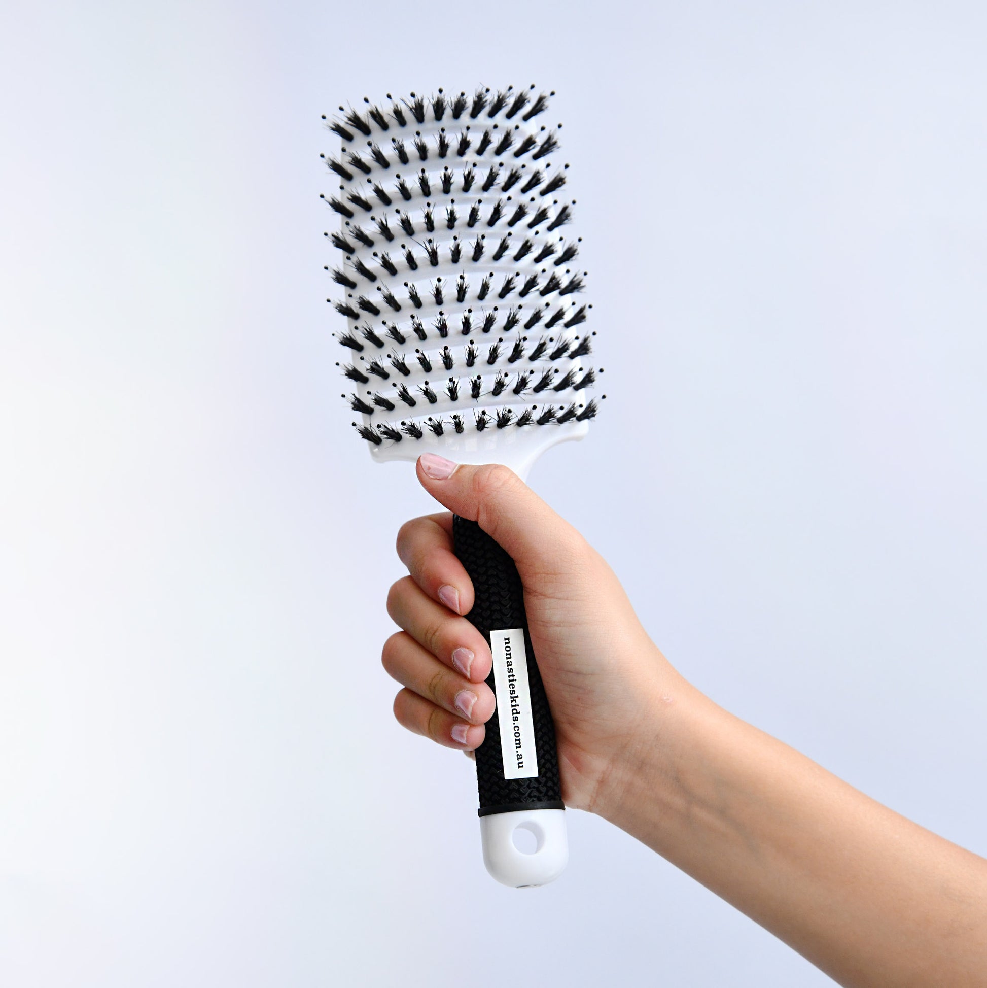 Hand holding a white hairbrush with bristle design against a light gray background