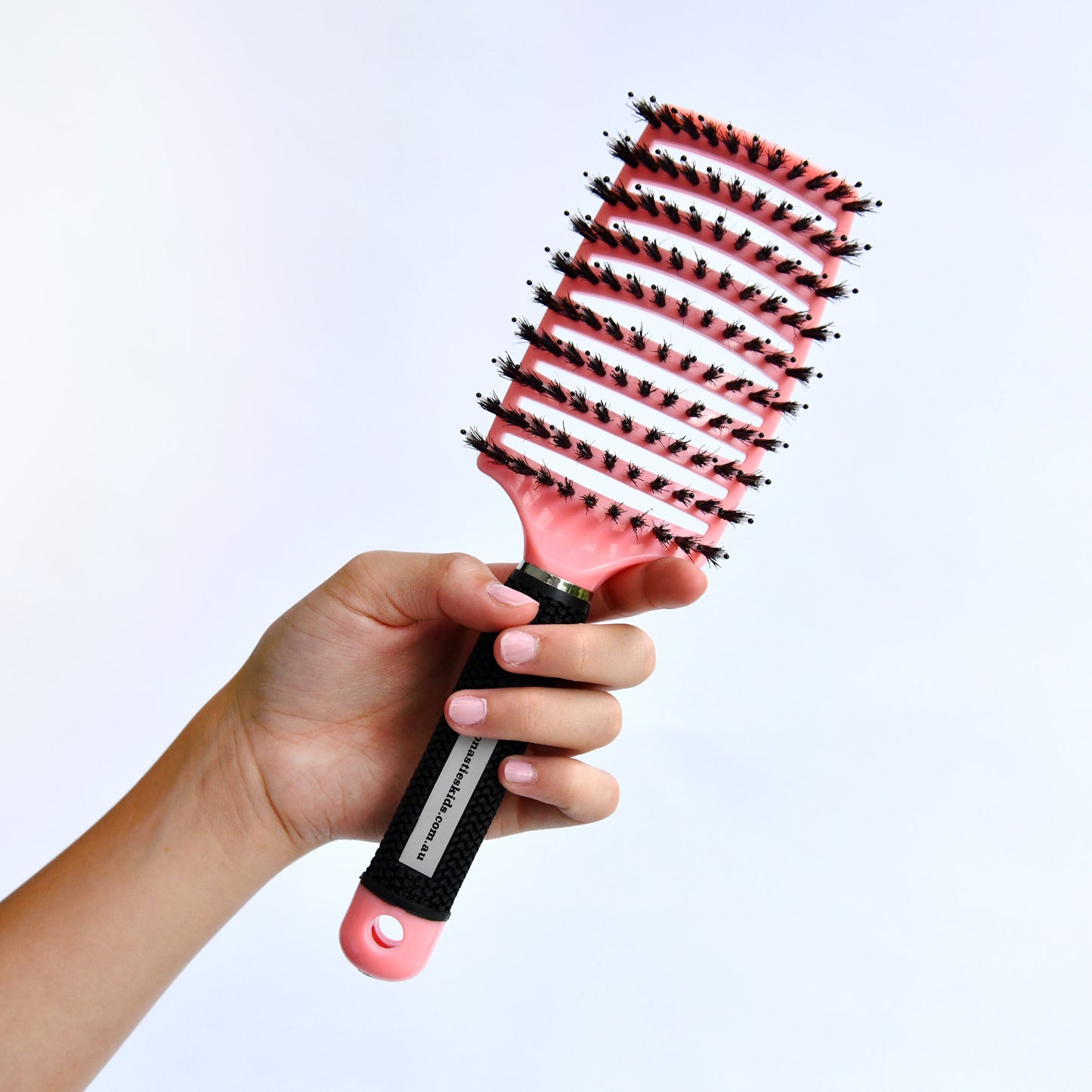 Hand holding a pink and black hairbrush against a light gray background