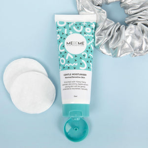 blue and white tube of gentle moisturiser for normal, sensitive and dry skin, with a blue lid. On a blue background with two cotton pads and a silver scrunchie.