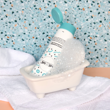 Load image into Gallery viewer, white tube of gentle cleanser for normal, sensitive or dry skin, with blue lid, with blue and black squiggles. Tube is sitting in a little bathtub with bubbles on a speckled background and white towel.
