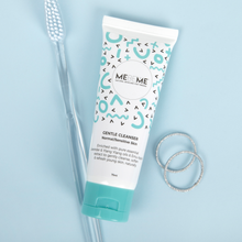 Load image into Gallery viewer, White tube of gentle cleanser for normal, sensitive and dry skin, with blue and black squiggles and a blue lid. To the left of the tube is a clear toothbrush and to the right of the tube is two silver rings. The background is blue.