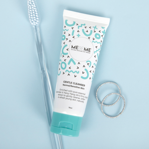 White tube of gentle cleanser for normal, sensitive and dry skin, with blue and black squiggles and a blue lid. To the left of the tube is a clear toothbrush and to the right of the tube is two silver rings. The background is blue.